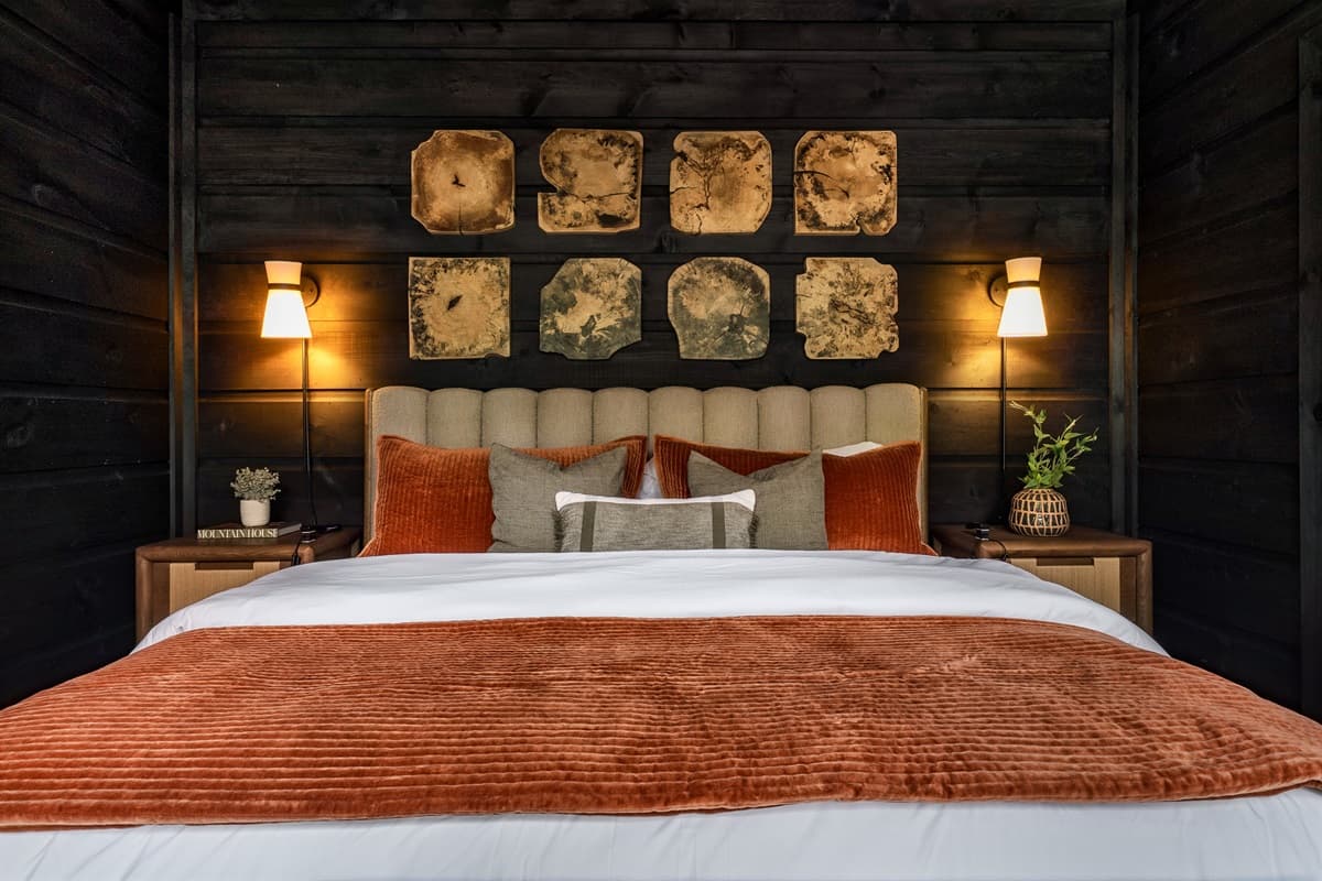 This inviting bedroom features a large, comfortable bed with warm-toned bedding and unique square wall art, framed by elegant wall sconces.