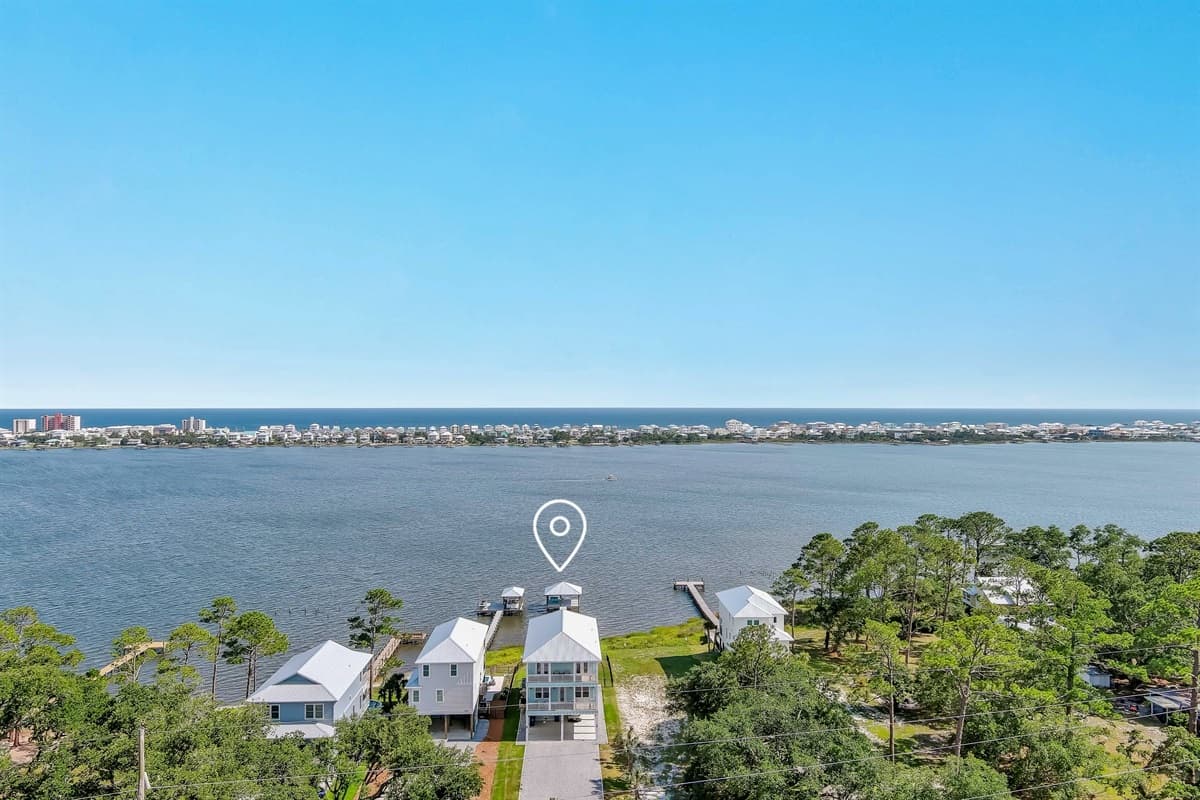 From this breathtaking aerial perspective, observe the harmonious blend of natural beauty and residential charm along the coastline, with private docks dotting the tranquil bay. The distant city lights add a touch of urban flair to this peaceful waterfront