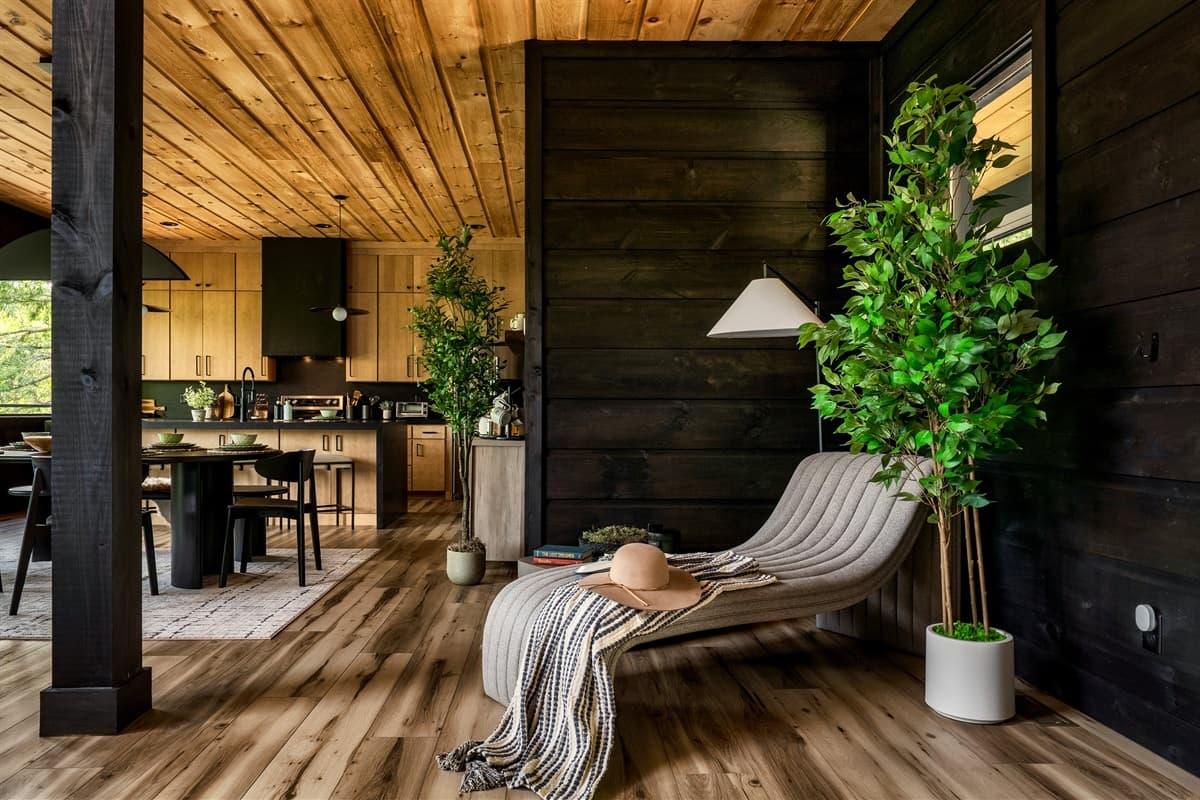 This inviting corner offers a perfect spot for unwinding, with a plush chaise lounge, natural light, and a view into the beautifully designed kitchen and dining area. The blend of modern comfort and rustic wooden elements creates a serene and stylish ambia
