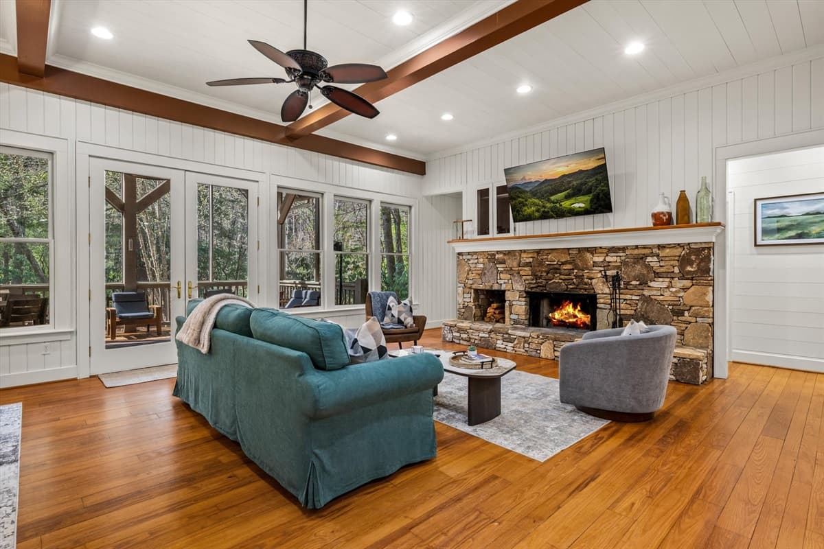 Living Room with TV Above the Stone Fireplace, Ceiling Fan and Forest Window Views