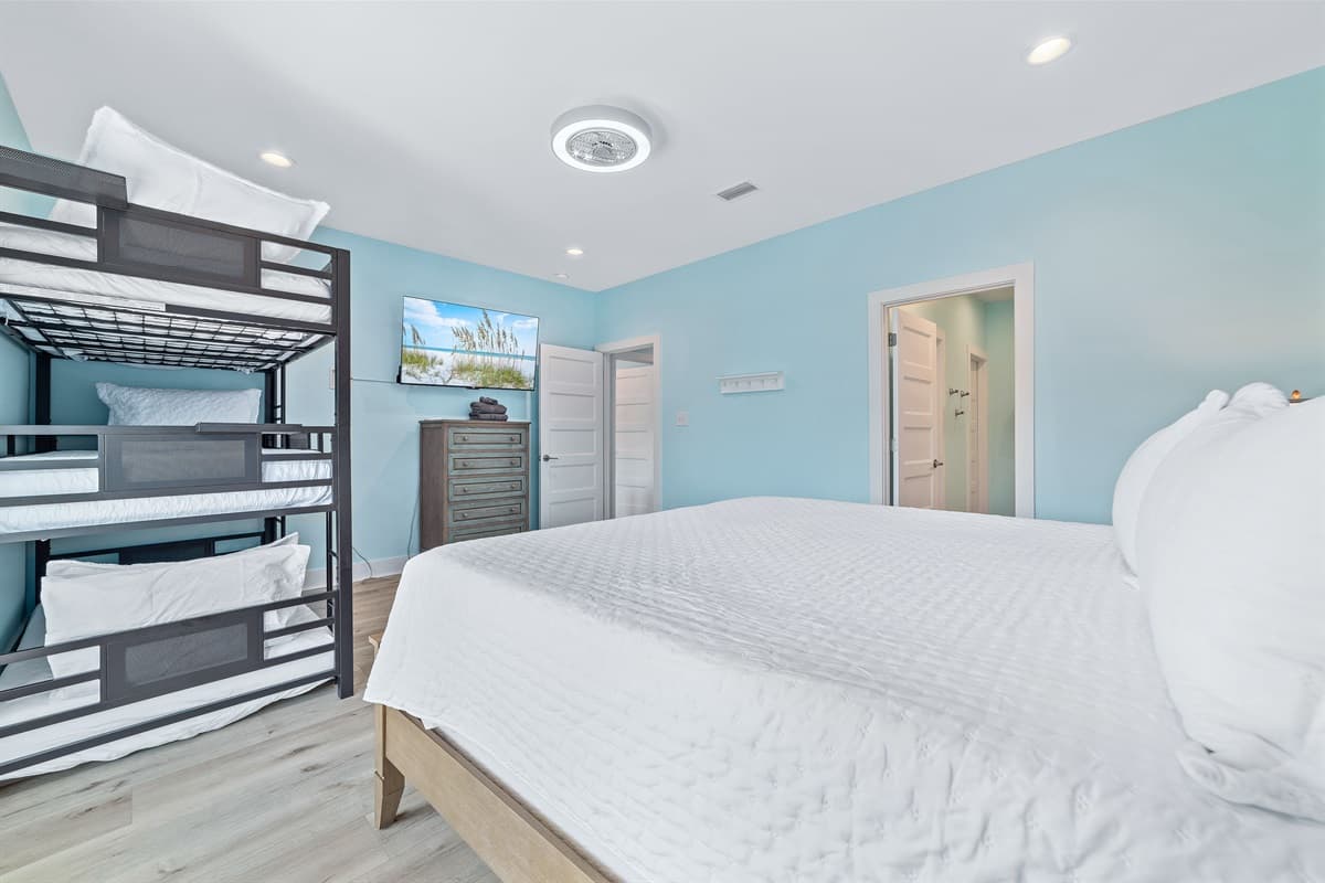This spacious bedroom offers flexible sleeping arrangements with a comfortable king-sized bed and a triple bunk bed, complete with a wall-mounted TV.
