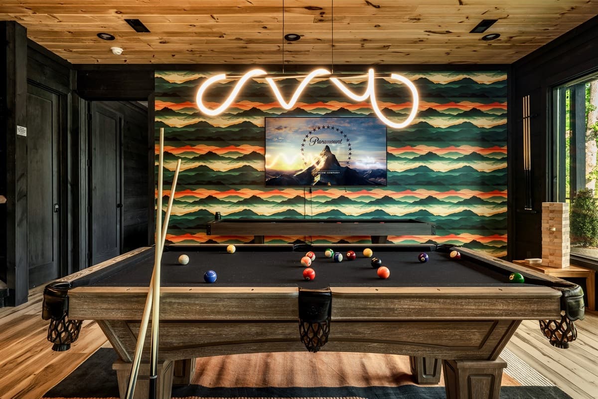 Enjoy endless entertainment in this stylish game room, complete with a professional billiard table ready for a lively game and a large screen for movie nights or sporting events. The striking horizontal striped wallpaper and custom neon lighting create a f