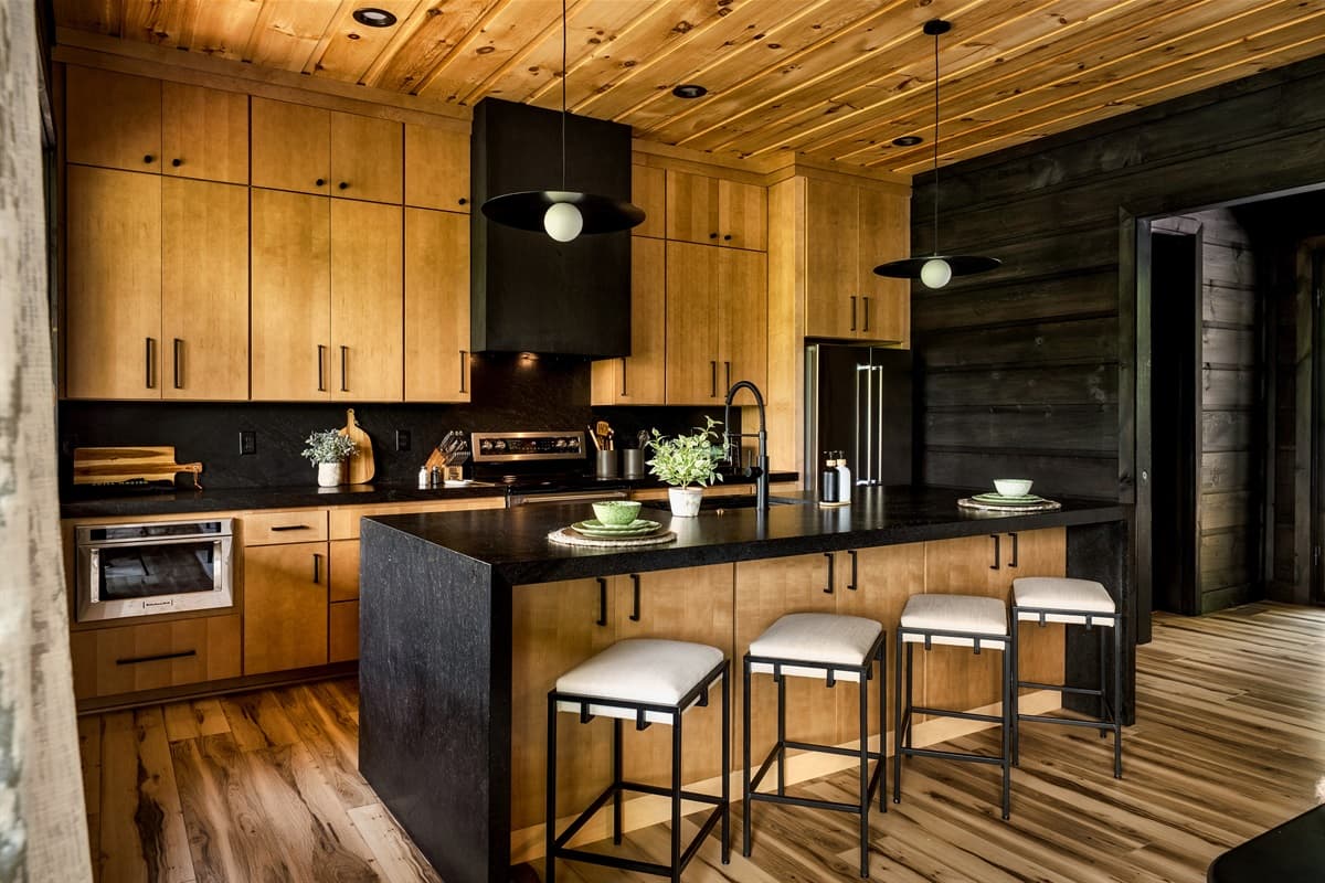 This spacious and stylish kitchen features abundant natural wood cabinetry, a large island with seating, and sleek black accents throughout.
