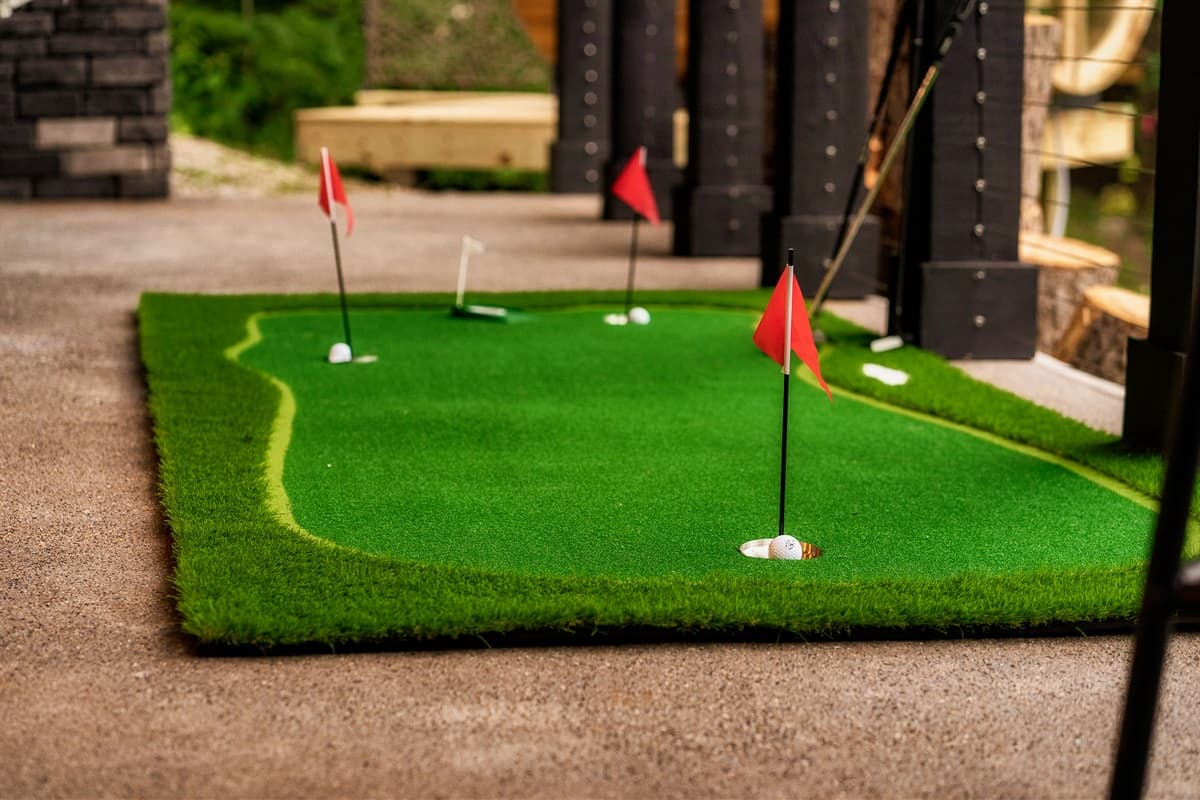 Practice your putting on this fun outdoor mini-golf green, complete with red flags and a vibrant artificial turf.