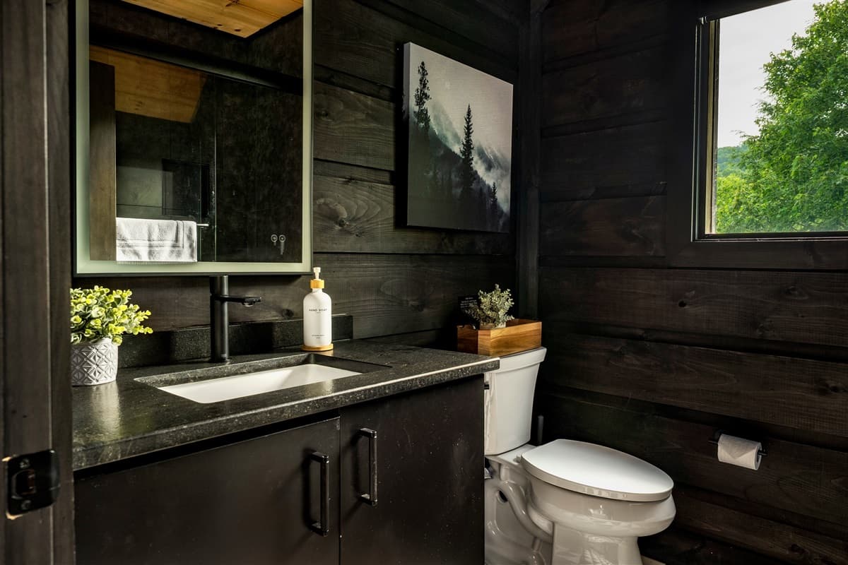 This well-appointed half bathroom features a modern vanity with a rectangular mirror and a scenic artwork, complemented by warm wooden walls.
