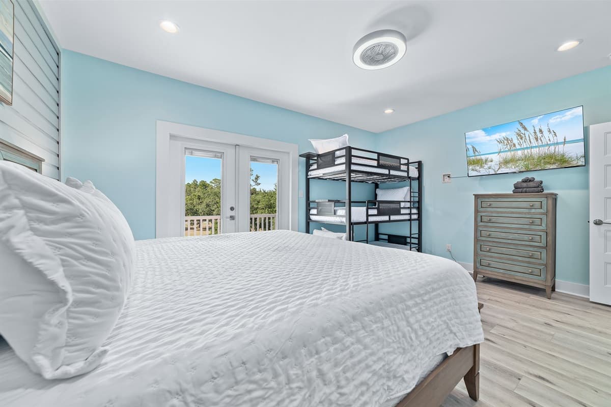 Ideal for larger groups or families, this inviting bedroom provides ample sleeping space with a plush king-sized bed and a sturdy bunk bed. A wall-mounted television offers entertainment, while French doors open to a private outdoor deck, inviting in the f