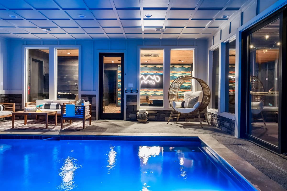 This stunning indoor pool area features a sparkling blue pool, ample lounge seating, and large windows that connect to the outdoor scenery.