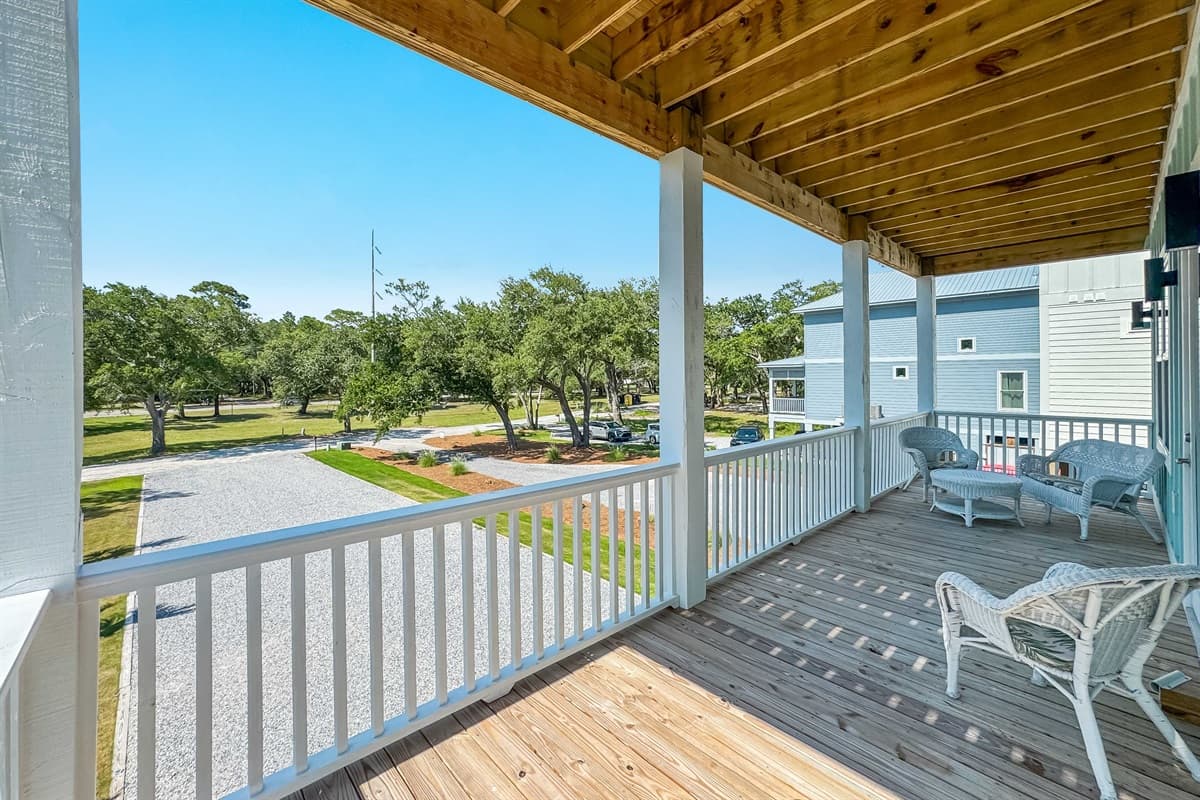 Enjoy the fresh air and tranquility on this inviting covered deck, featuring comfortable wicker chairs and a matching table, perfect for morning coffee. It provides an ideal vantage point to take in the serene landscape and distant homes.