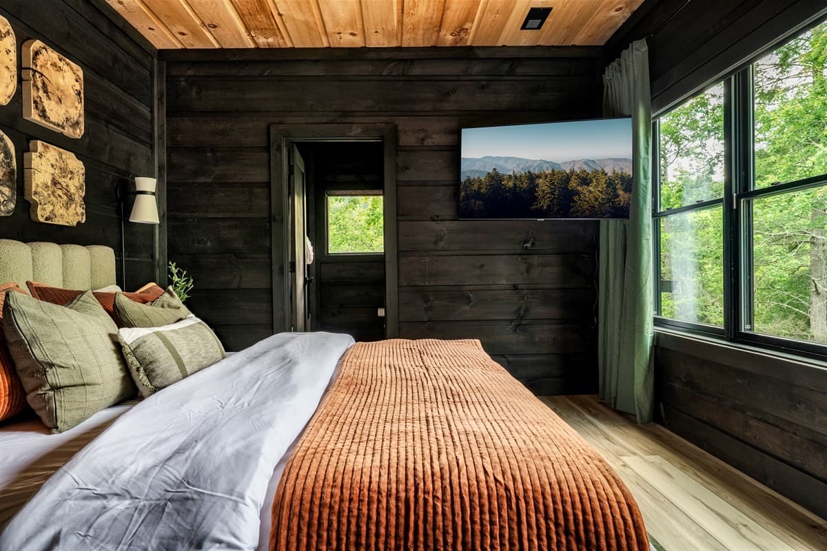 This inviting bedroom offers a comfortable bed, stylish wall decor, and a mounted television, all set against a backdrop of natural wood paneling.