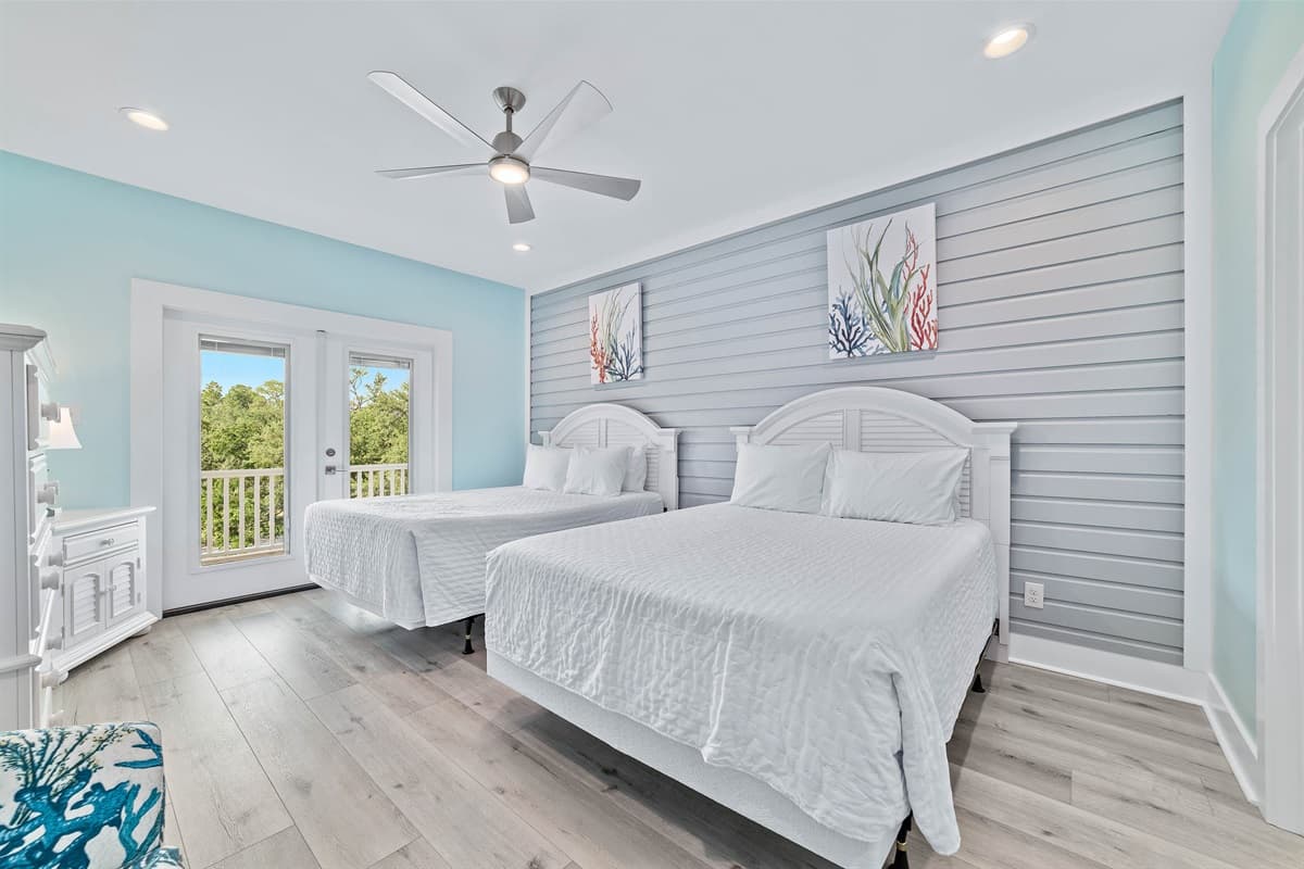 This bright bedroom features two comfortable queen-sized beds, a soothing shiplap accent wall, and direct access to an outdoor deck.