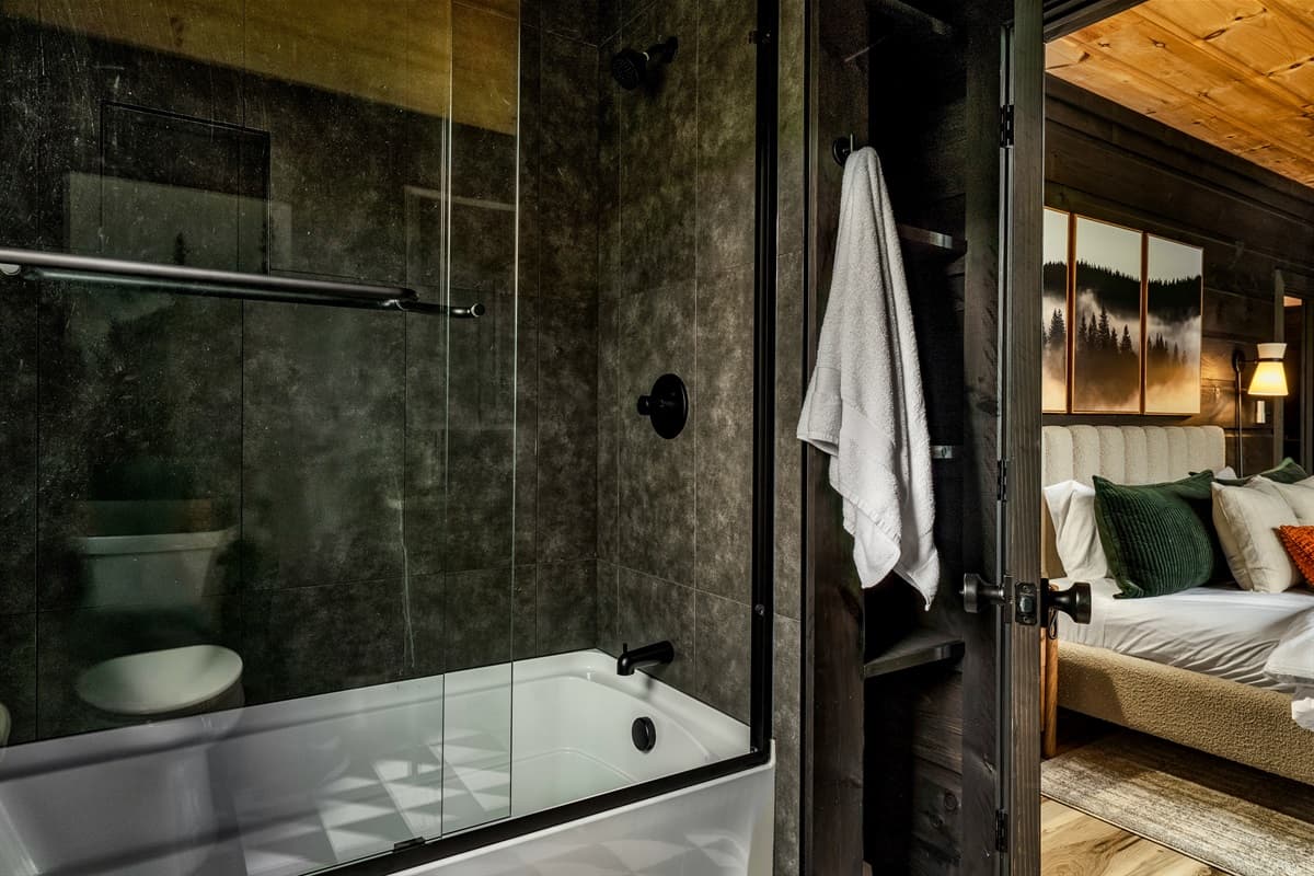 This modern bathroom features a sleek shower-tub combination and dark tiled walls, offering direct access to a beautifully appointed bedroom.