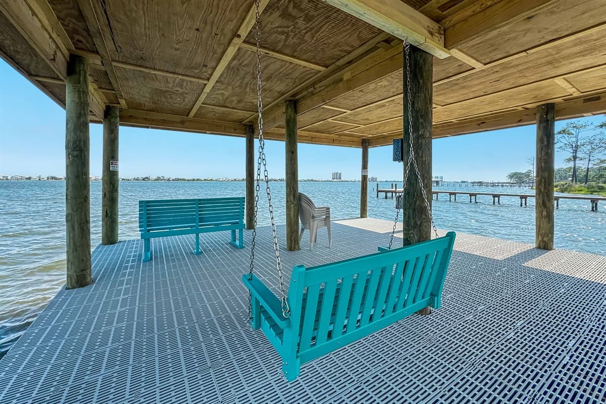 Relax and enjoy the waterfront breeze from the private covered area under the house, featuring a comfortable swing and bench seating.