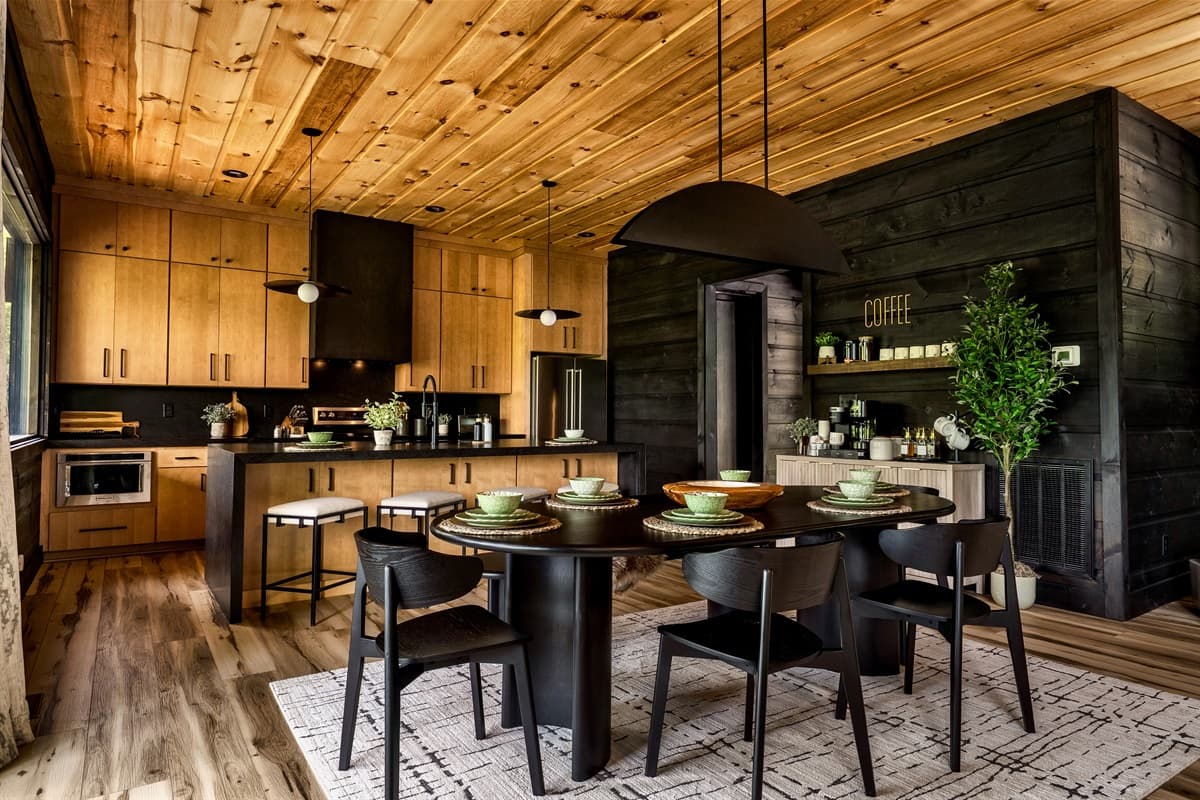 This modern kitchen and dining area boasts rich wooden cabinetry and ceilings, black accents, and an inviting round dining table.