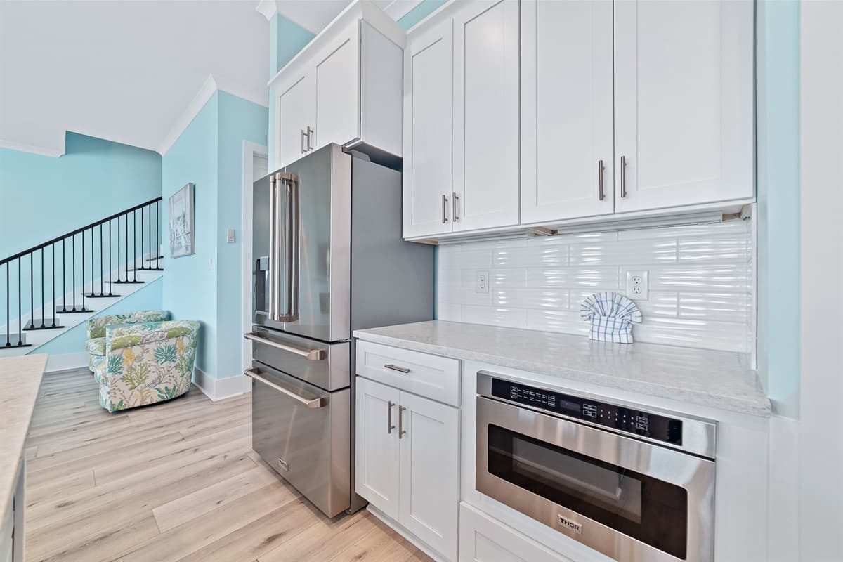 The bright kitchen features white cabinetry and a convenient built-in microwave, connecting to an open living space with stairs.