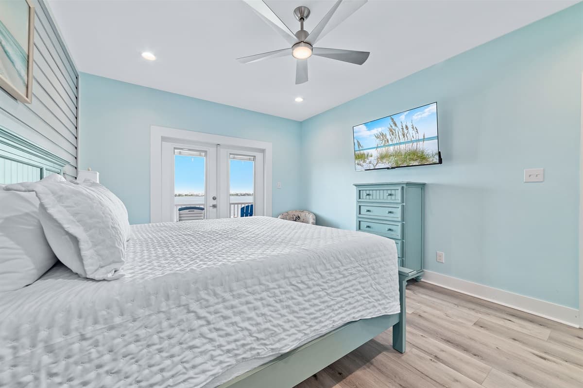 Unwind in this spacious bedroom, offering a plush king-sized bed and a convenient wall-mounted television for entertainment. French doors open directly onto a private outdoor deck, allowing you to easily step outside and enjoy the fresh air and views.