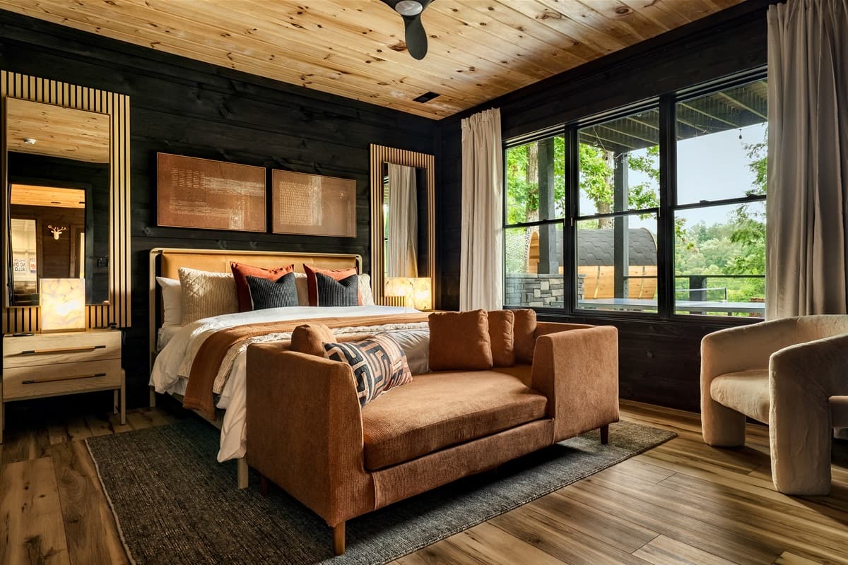 This luxurious bedroom features a large, comfortable bed, a stylish accent sofa, and expansive windows offering views of the surrounding nature.