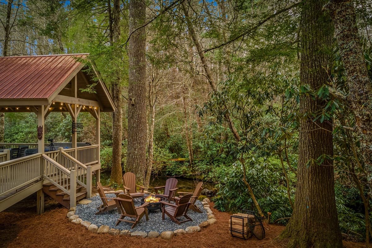 Fire Pit and Adirondack Chairs Directly on the River with the Gazebo and String Lights Behind