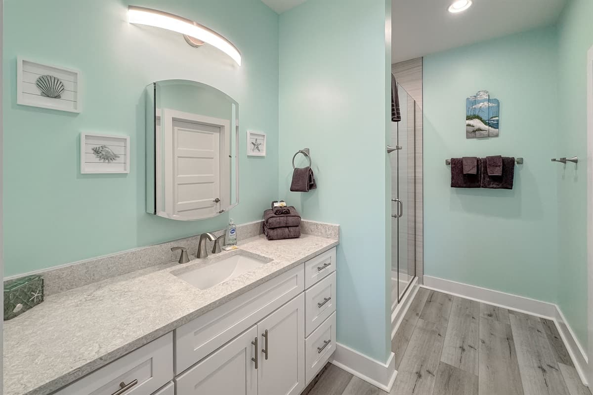 Step into this clean and inviting bathroom, complete with a contemporary white vanity, a wide mirror with modern lighting, and light green walls. The spacious walk-in shower boasts elegant tiled walls and a convenient built-in niche, providing a luxurious