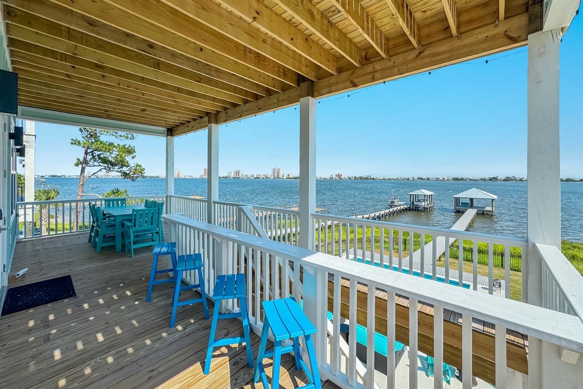 Enjoy an unparalleled outdoor experience on this spacious covered deck, featuring a vibrant turquoise dining set perfect for al fresco meals and an inviting bar area with stools. From this vantage point, you'll have breathtaking views of the waterfront, th
