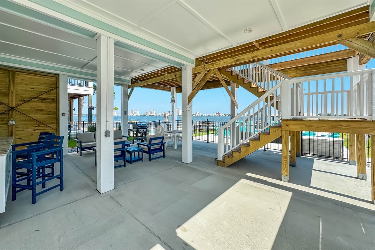 This spacious covered outdoor patio features multiple comfortable seating areas, a convenient wet bar, and a set of stairs leading to upper levels, all with water views.