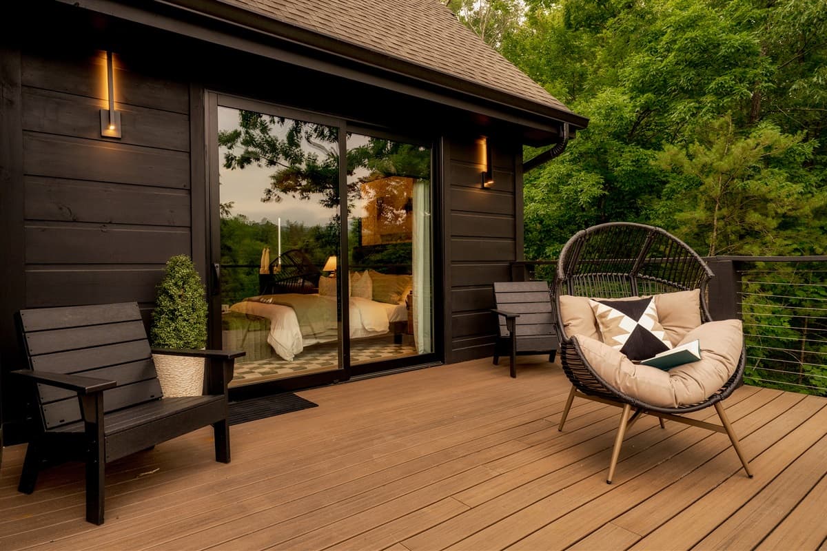 This inviting outdoor deck, accessible through large glass sliding doors, features a comfortable egg chair and additional seating, perfect for enjoying the serene wooded surroundings.
