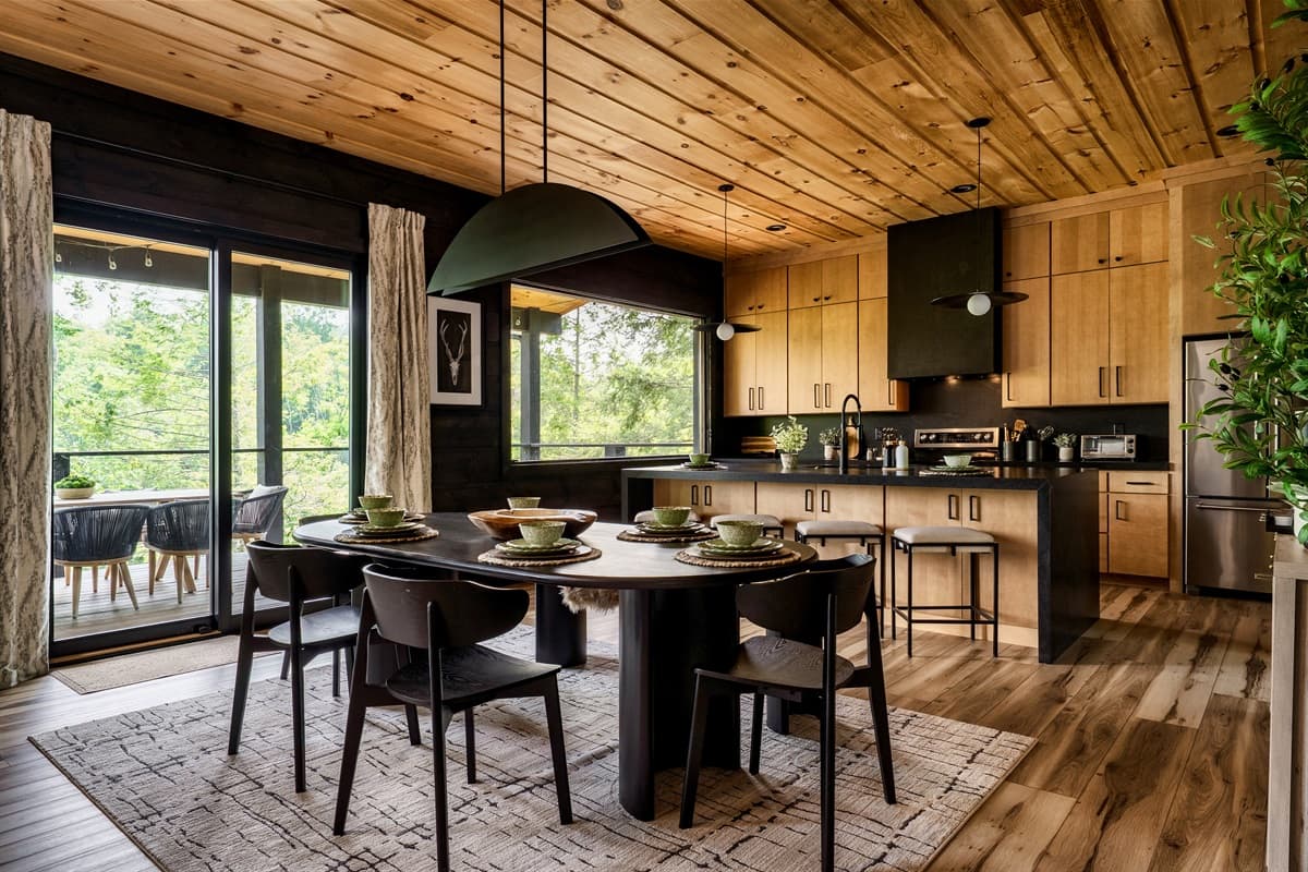 This spacious open-concept area combines a modern kitchen with natural wood accents and a stylish dining space leading to an outdoor deck.