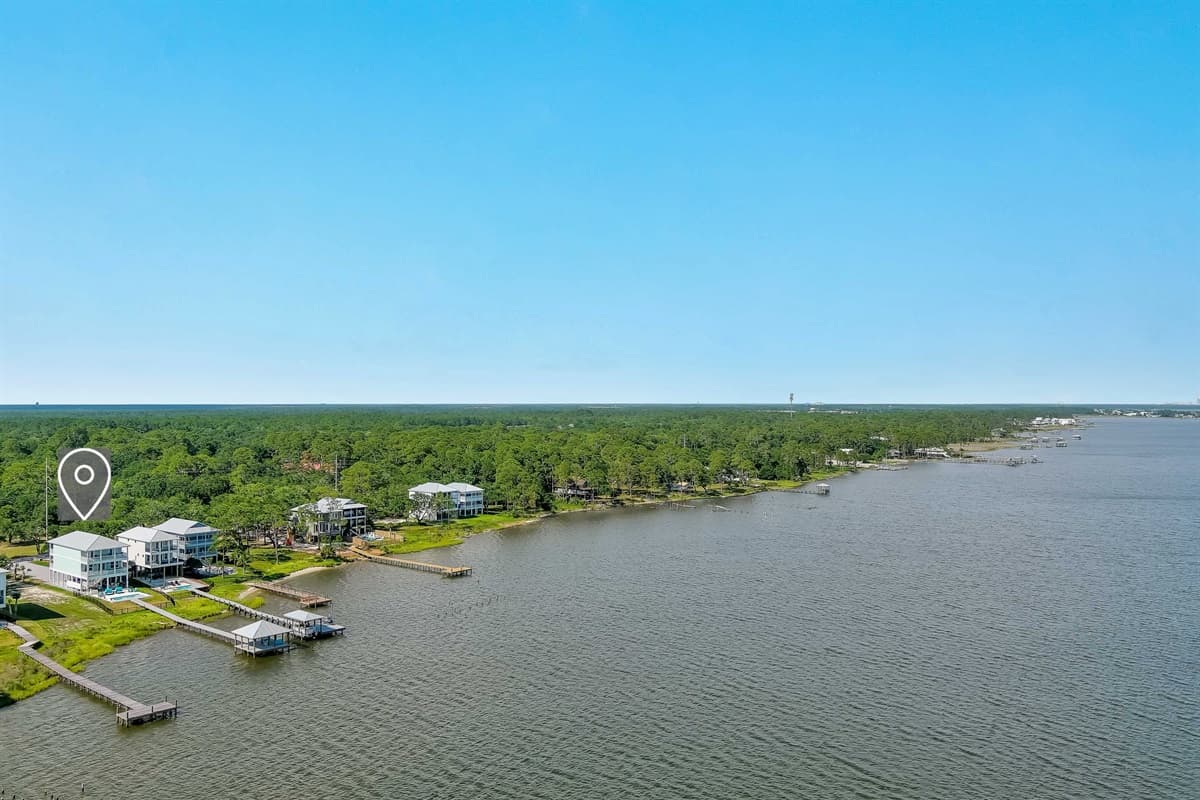 This expansive aerial view showcases a serene coastal landscape with a cluster of waterfront homes, lush green trees, and private docks extending into the bay.