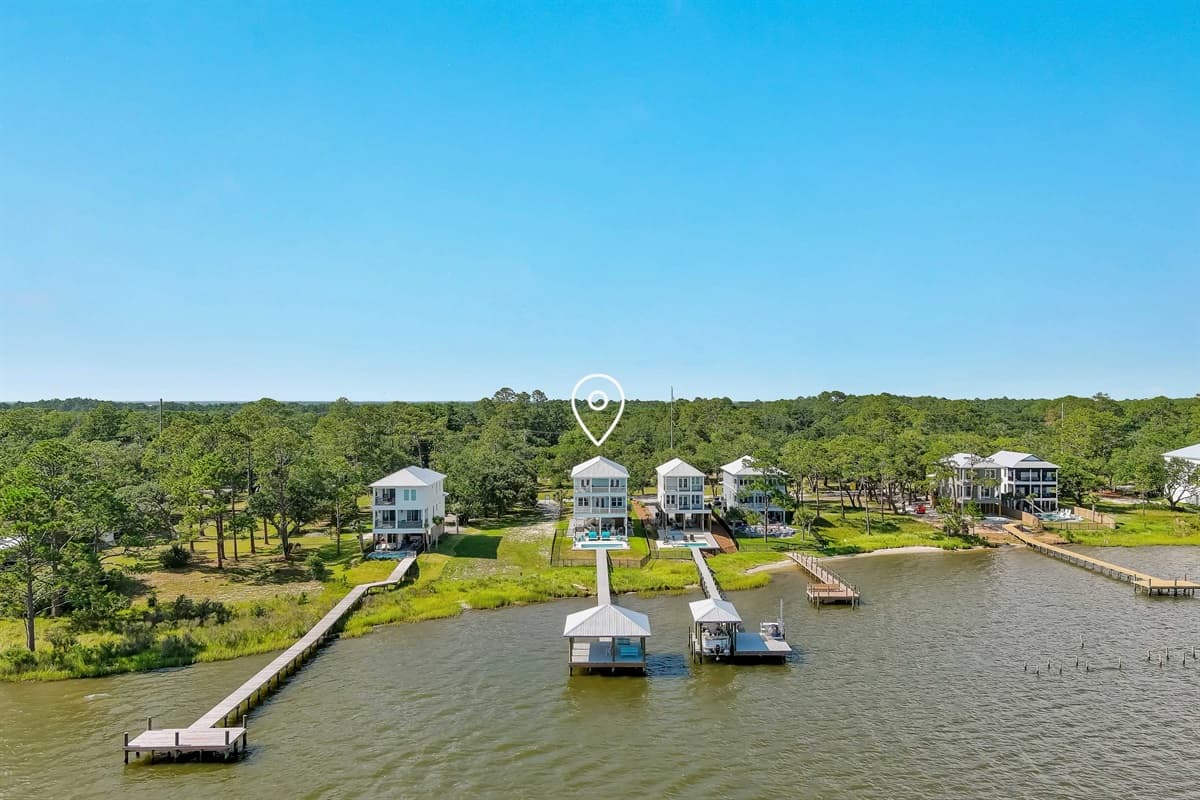 This stunning aerial view captures a cluster of elevated coastal homes along the tranquil bay, each with a private dock extending into the water.