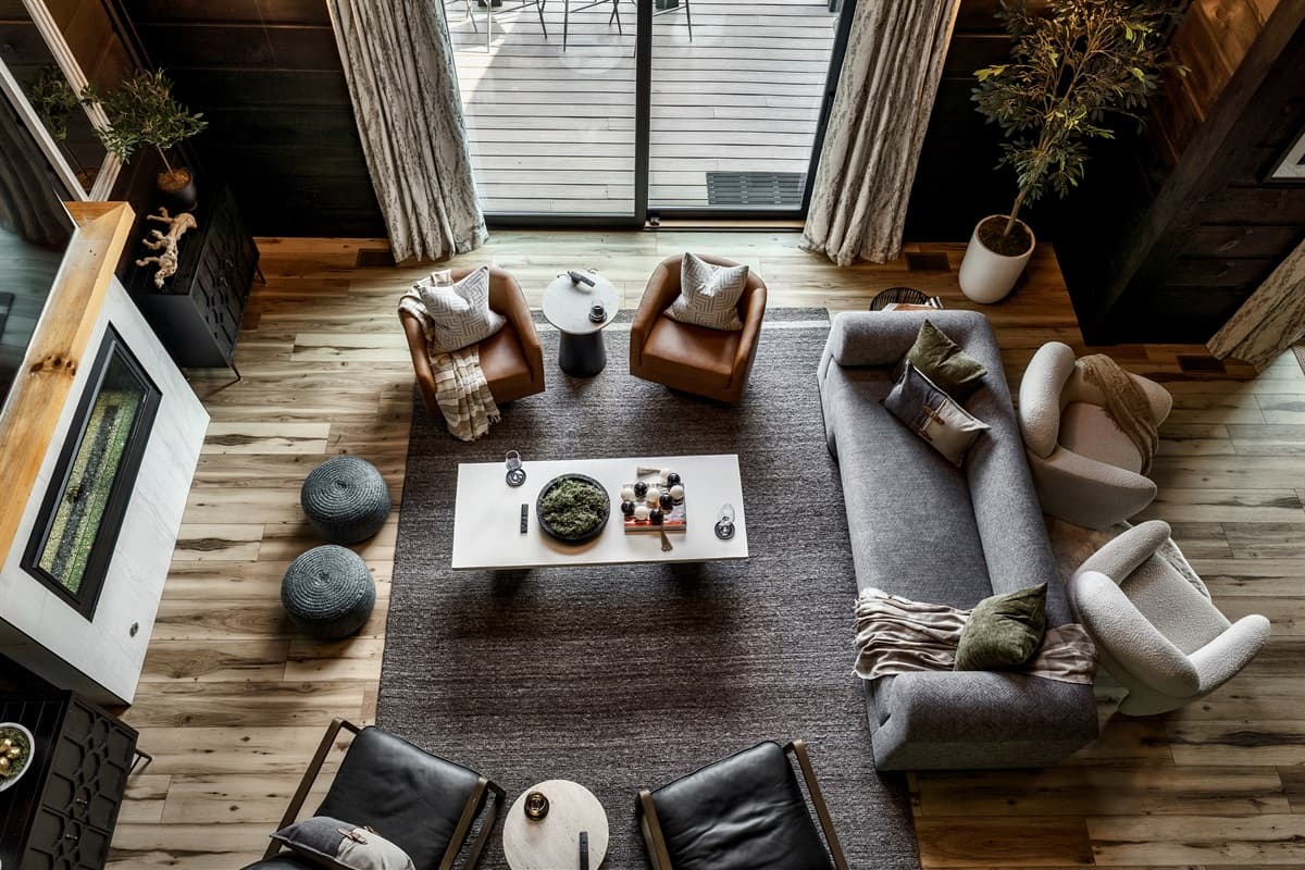 Experience the cozy ambiance of this beautifully arranged living space from an elevated perspective, showcasing a thoughtful layout with a large area rug, a stylish coffee table, and comfortable seating. The warm wooden floors and ceilings, combined with t