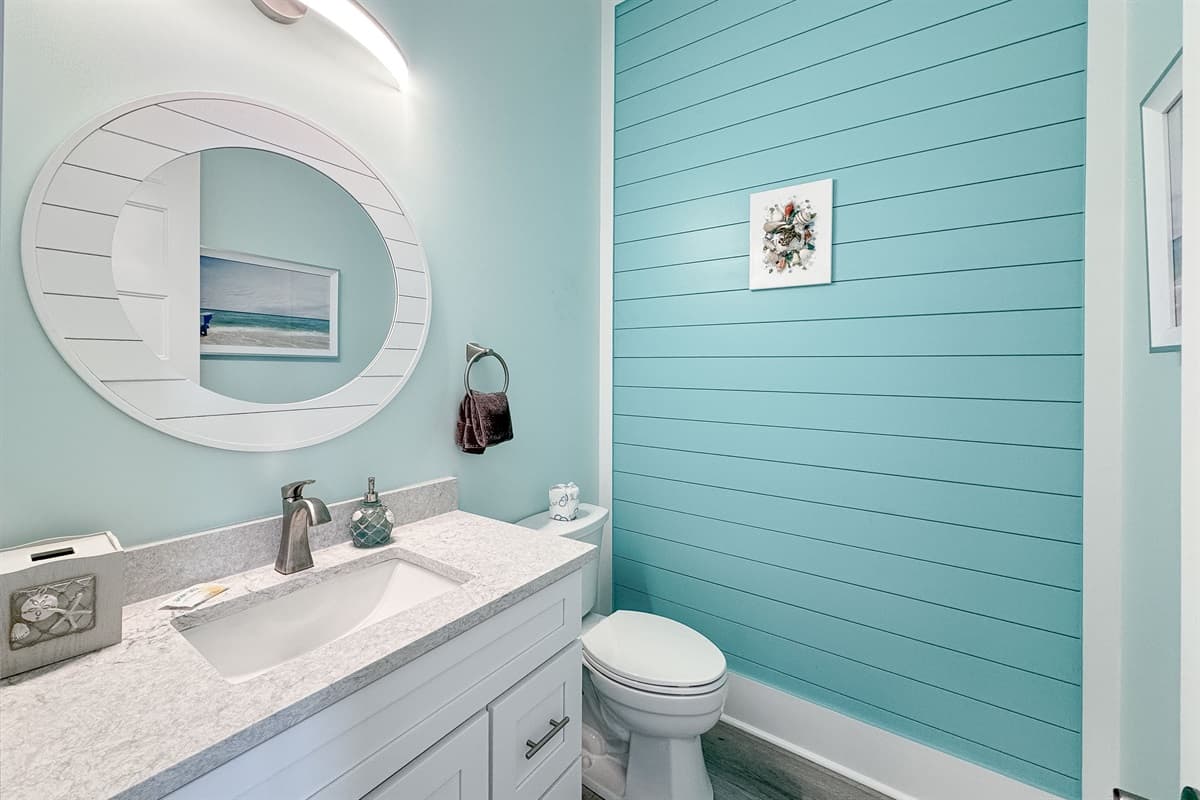 Step into this stylish bathroom, featuring a clean white vanity with ample counter space and a large circular mirror. The vibrant blue shiplap accent wall adds a touch of coastal charm, creating a refreshing and inviting space.