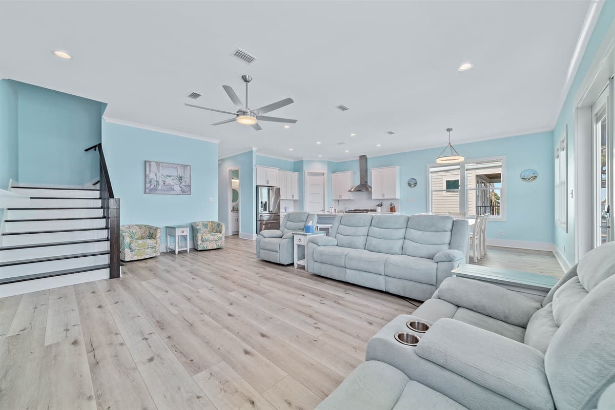 This bright and inviting open-concept space combines a comfortable living room with plush sofas, a large wall-mounted television, and a stylish electric fireplace. Its seamless flow into the modern kitchen and dining areas creates a perfect setting for bot