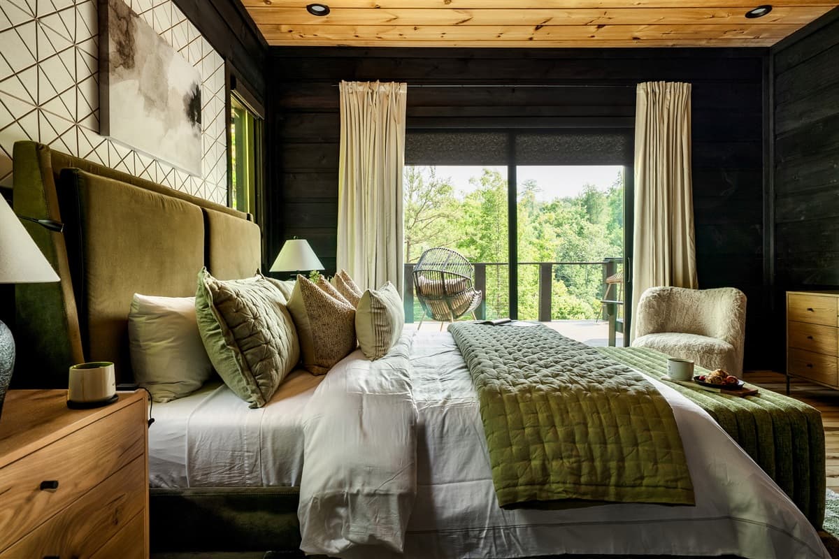 This inviting bedroom features a large, comfortable bed with an elegant upholstered headboard and direct views of the natural surroundings.
