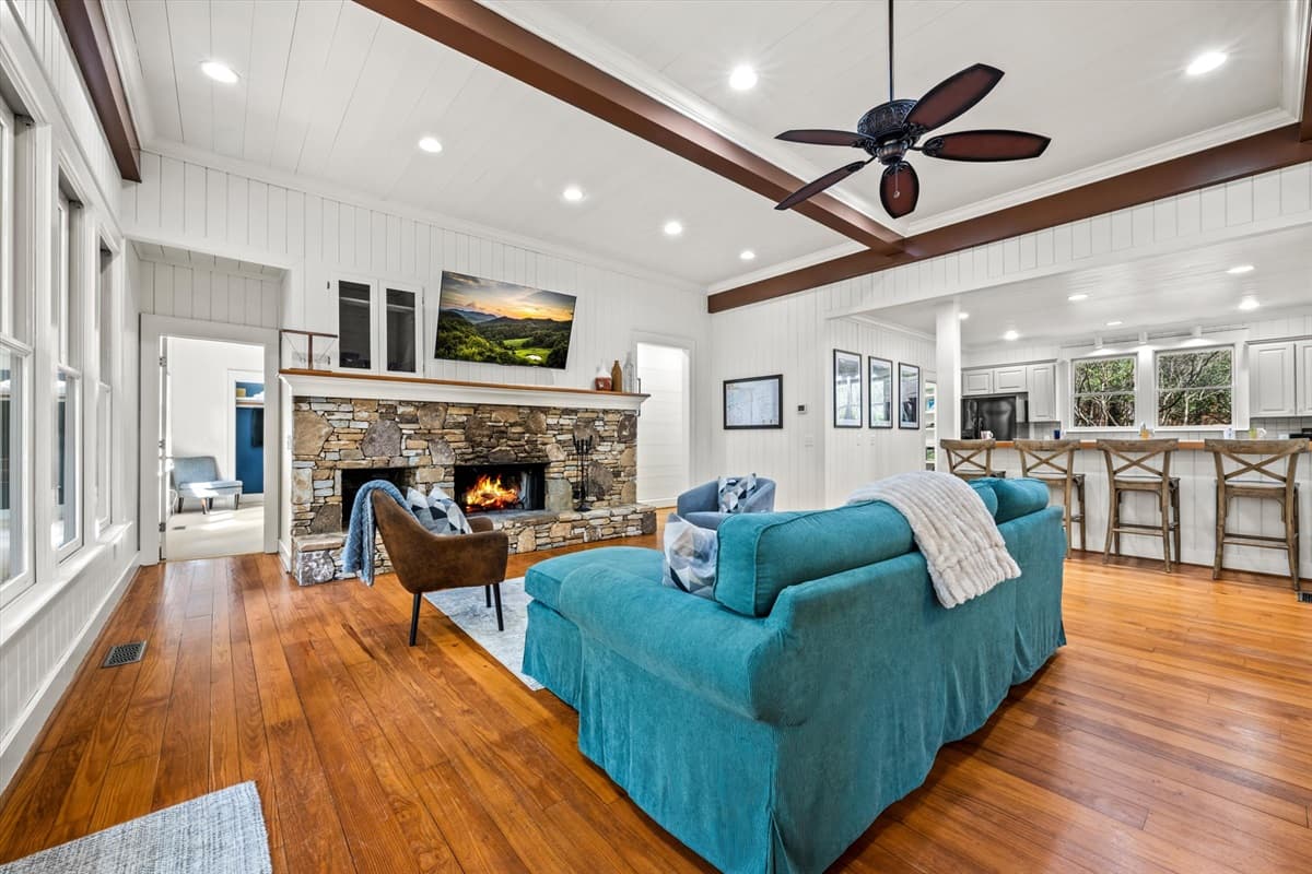 Spacious Living Room with Turquoise Sofa, Ceiling Fan, Exposed Beams and Stone Fireplace