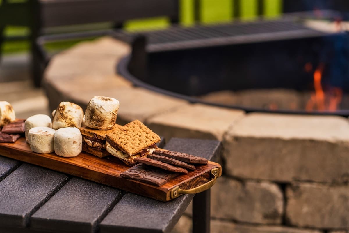 Gather around the cozy outdoor fire pit and indulge in the timeless delight of s'mores, with marshmallows, chocolate, and graham crackers perfectly arranged on a rustic wooden board. It's an ideal setting for creating sweet memories under the stars.