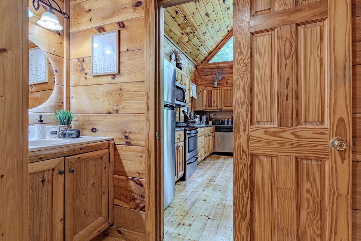 From this well-appointed bathroom, you get a glimpse into the cabin's main living area, featuring a full kitchen and continuous warm wood walls. It highlights the functional layout and consistent charming aesthetic of the home.