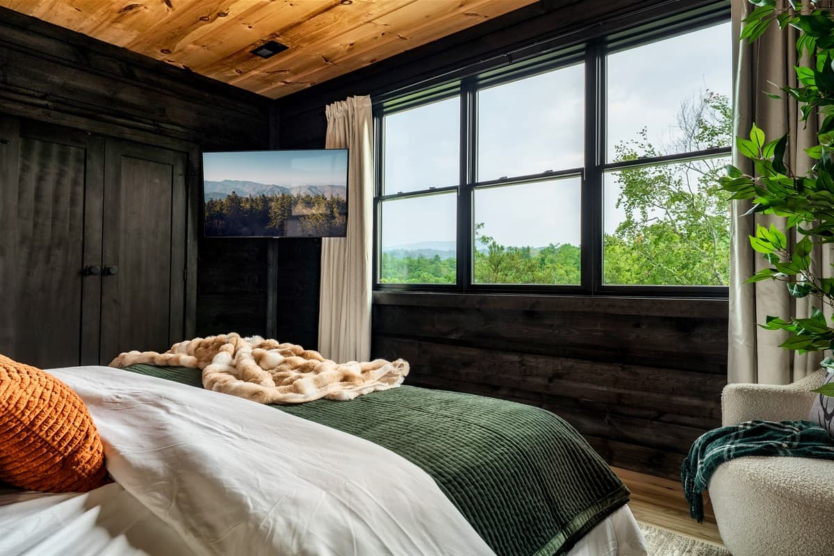 Unwind in the comfort of this inviting bedroom, where a large, cozy bed is complemented by a sleek wall-mounted TV for your viewing pleasure. The room's design seamlessly integrates with nature through vast windows, allowing you to enjoy the stunning natur