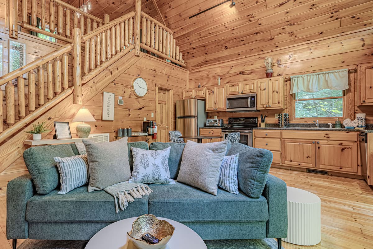 Relax in the comfortable living area, featuring a plush sofa and views of the cabin's open layout and rustic staircase.