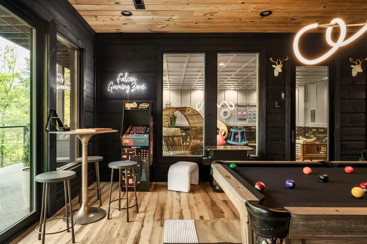 This exciting game room features a full-sized billiard table, an arcade machine, and a high-top bar table, all illuminated by unique neon lighting.