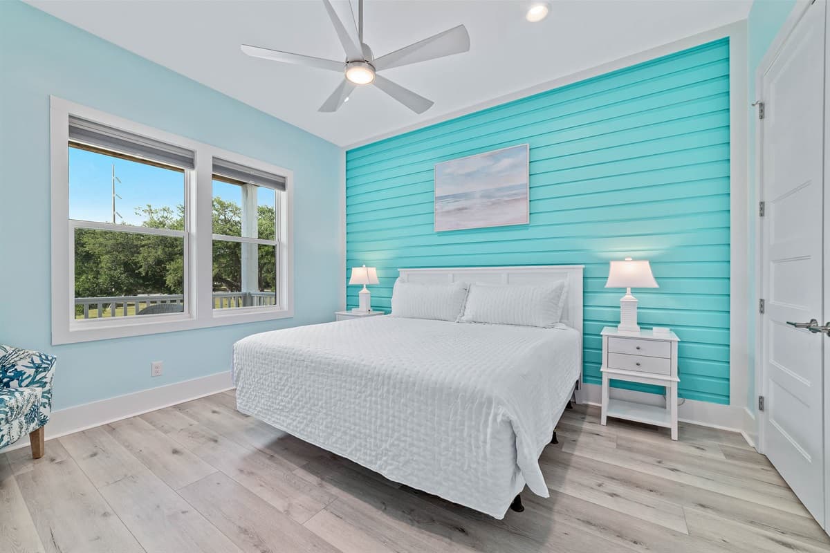 This bright and comfortable bedroom features a queen-sized bed, a ceiling fan, and a striking blue shiplap accent wall.