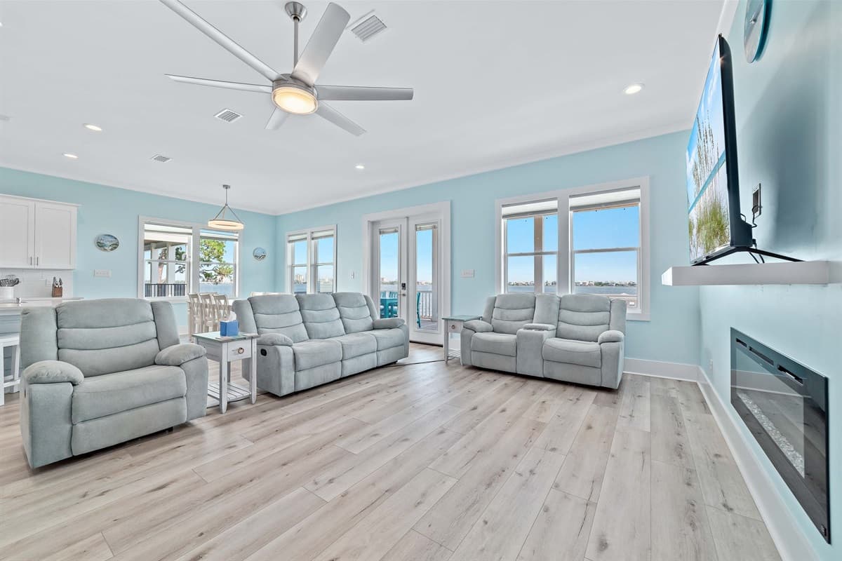 The bright and spacious living area offers comfortable seating, a large wall-mounted TV, and direct access to an expansive outdoor deck.