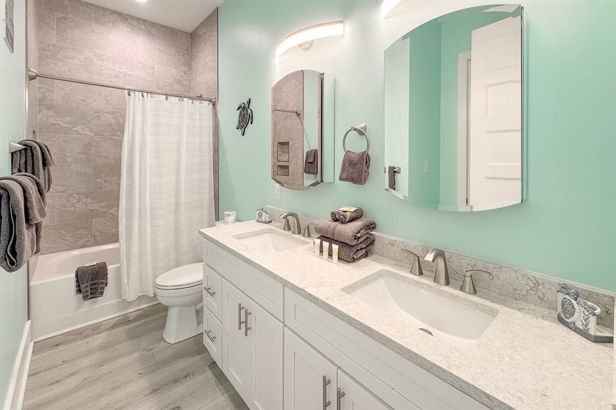 Enjoy the convenience of this spacious bathroom, which boasts a double vanity with two sinks, bright lighting, and a combination bathtub and shower with elegant tile surround. It's designed for comfort and functionality for multiple guests.