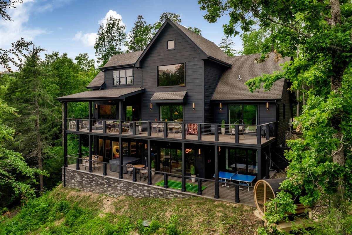 Experience modern living in this striking dark-toned residence, which boasts multiple tiers of spacious outdoor decks furnished with comfortable seating, perfect for entertaining or unwinding amidst nature. The thoughtful design seamlessly blends indoor an