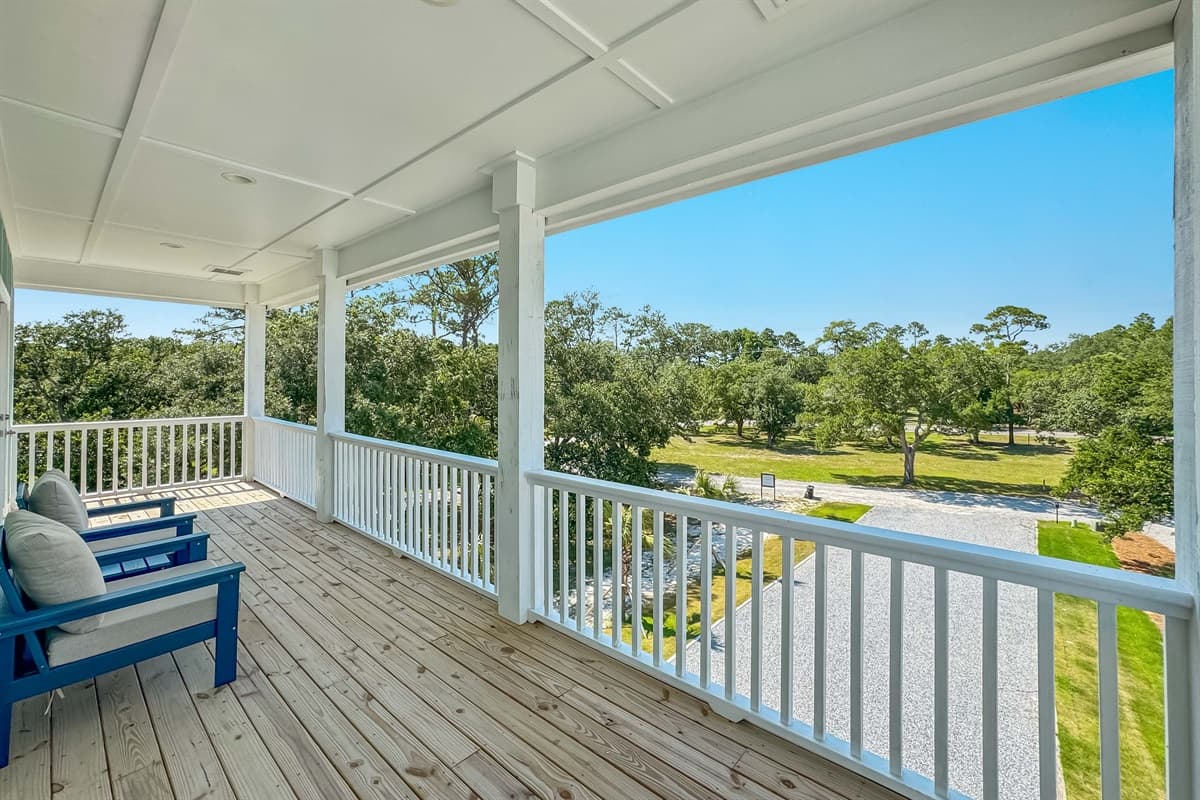 This spacious outdoor deck provides a perfect setting for enjoying fresh air and the tranquil surroundings, featuring comfortable blue armchairs under a wide covered area. It's an ideal spot for unwinding, with picturesque views of lush greenery.