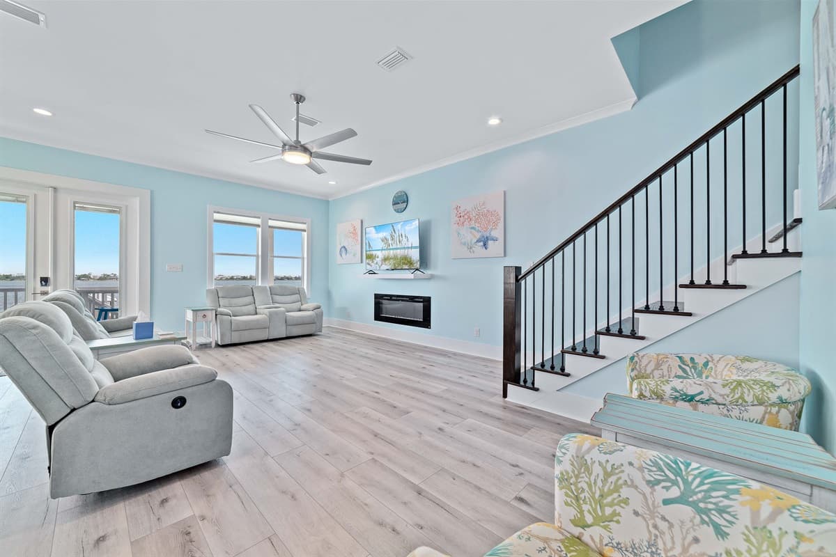 The bright and airy living room offers comfortable seating, a flat-screen TV above a modern fireplace, and direct access to an outdoor area.
