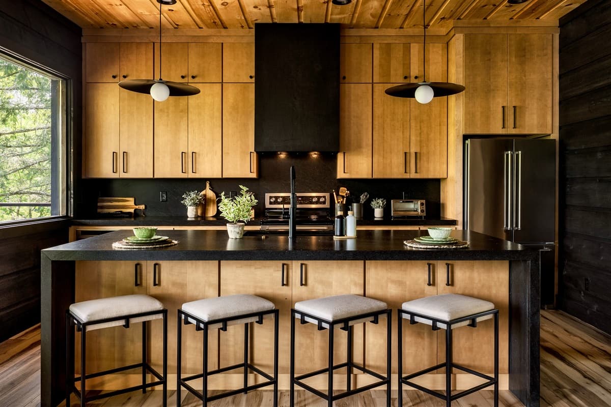 Prepare meals in style in this beautifully designed kitchen, featuring warm natural wood cabinets, dark countertops, and contemporary black fixtures. The large island with chic bar stools offers a perfect spot for casual dining or engaging with the chef.