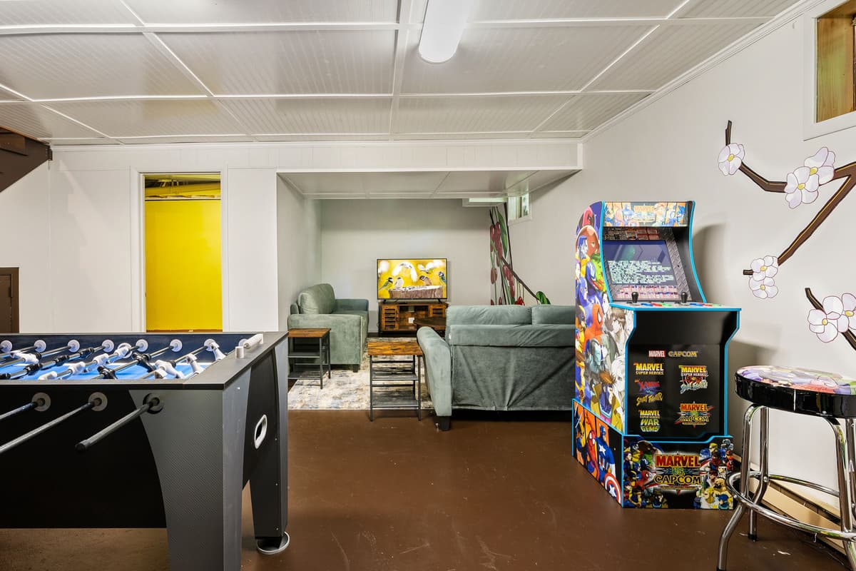 Head downstairs for a fun-filled game room featuring a TV, foosball table, and arcade machine, perfect for relaxing and enjoying some friendly competition.