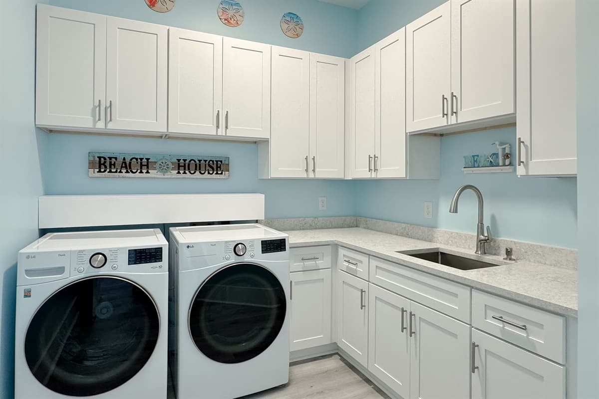 The well-equipped laundry room features a washer and dryer, ample white cabinetry, and a convenient sink with a faucet.