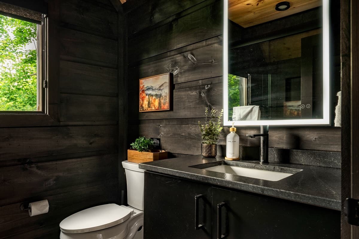 This modern bathroom features a stylish vanity with a lighted mirror and a window offering a lush green view.