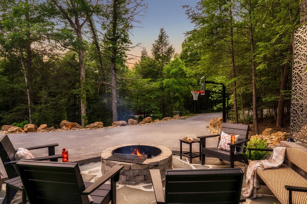 Enjoy an evening under the stars around this cozy fire pit, complete with ample seating and surrounded by the serene wooded landscape. The adjacent paved area and basketball hoop provide additional entertainment options, perfect for family fun.