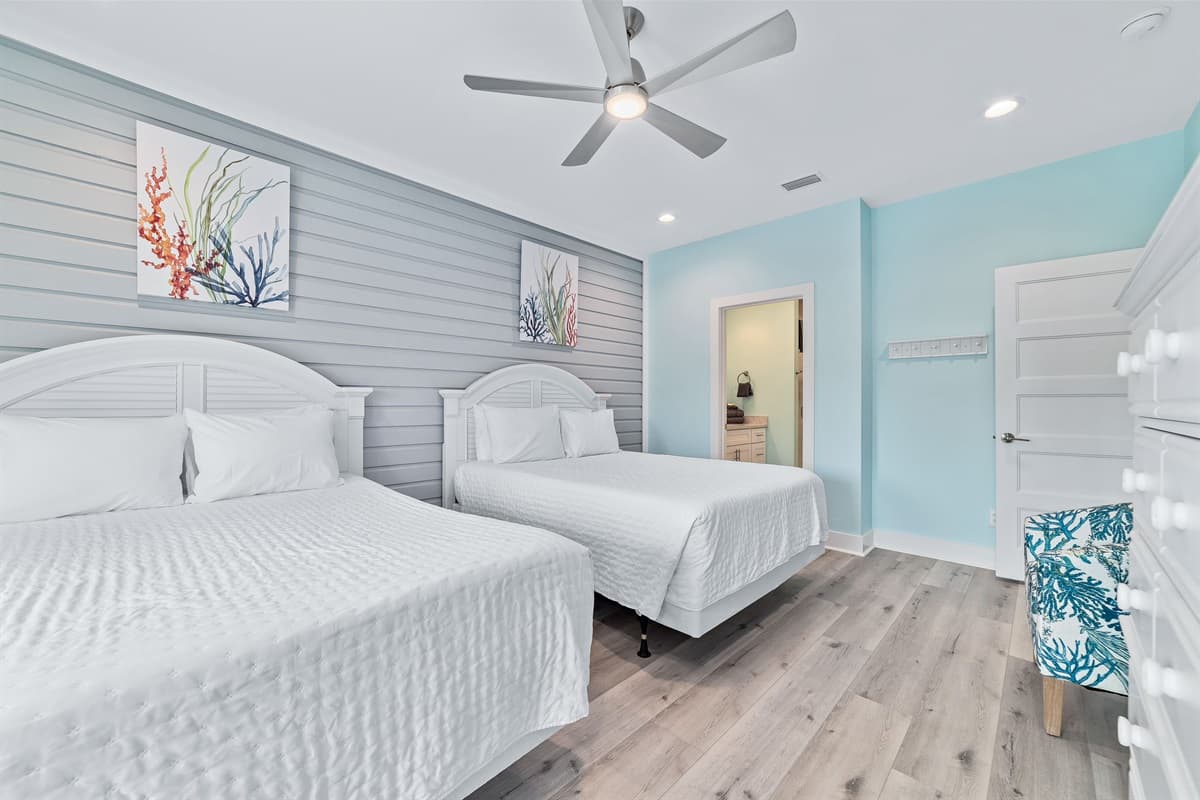 This bright bedroom features two comfortable queen-sized beds, a stylish shiplap accent wall, and access to a private bathroom.